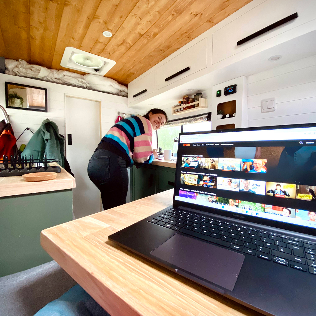 Emily standing in the campervan with a laptop on the table in the foreground